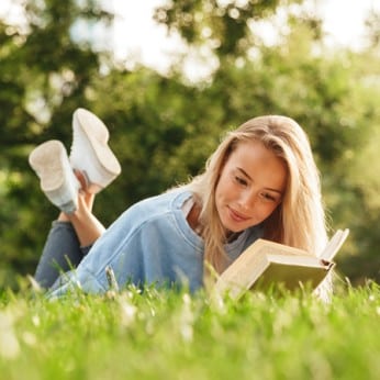 Frau mit Buch liegt entspannt auf einer WIese